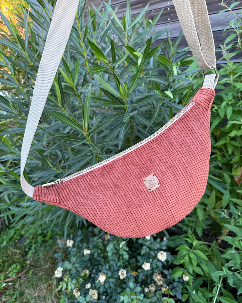 Terracotta Corduroy Belt Bag with its beige strap, hanging among green plants